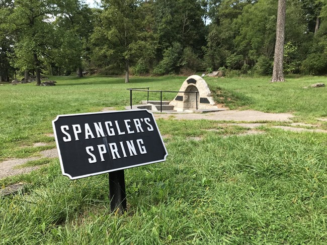 A granite and stone archway surrounds a natural spring, set down in a few steps; a black iron tablet in front reads "Spangler's Spring"
