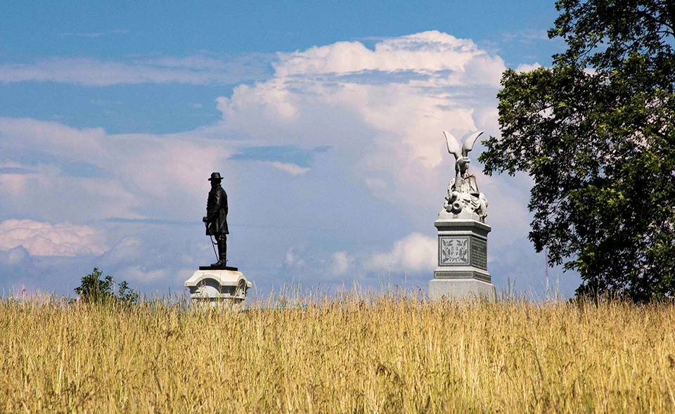 Two monuments on Oak Ridge. A blue sky with puffy white clouds can be seen behind two monuments at the horizon line with a wheat field in the foreground.