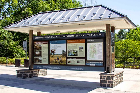 An information kiosk with a silver roof shows five different panels with information about the Museum and Visitor Center.