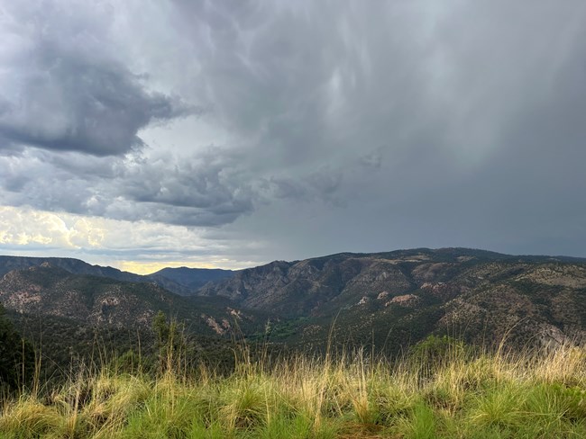 A landscape image of a mountain and canyon with storm clouds lurking in the background