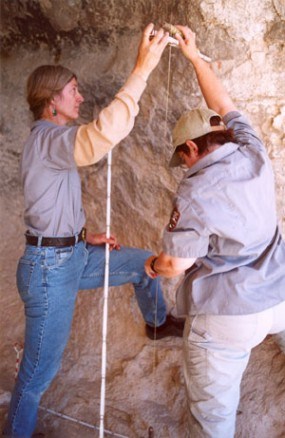 A photo of archeologists measuring the side of a cave wall. A photo of archeologists measuring the side of a cave wall.