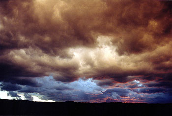 A photo of various layer of colored clouds visable over the monument near nightfall.