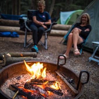 Two people sit next to a campfire.