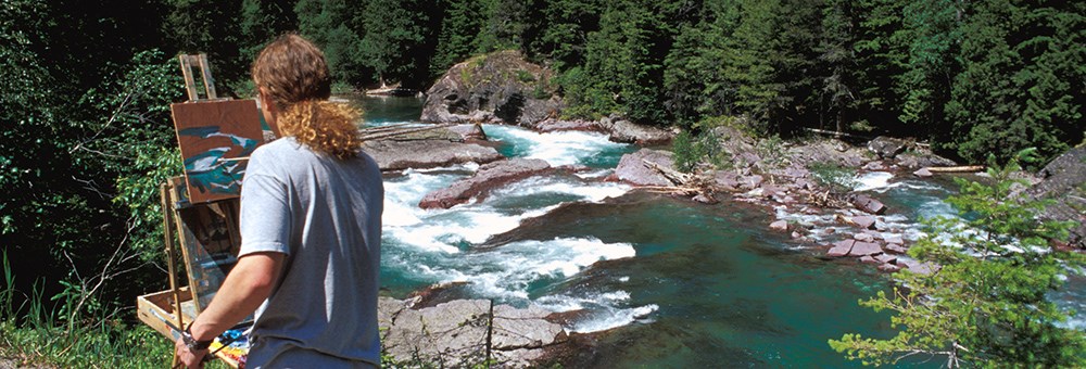 curly haired man paints at easel by creek curly haired man paints at easel by creek