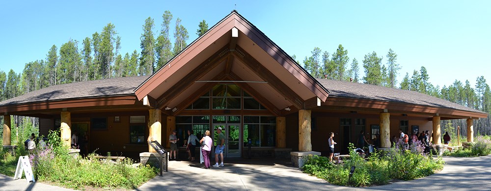 people mill about wide building with pitched roof over entry