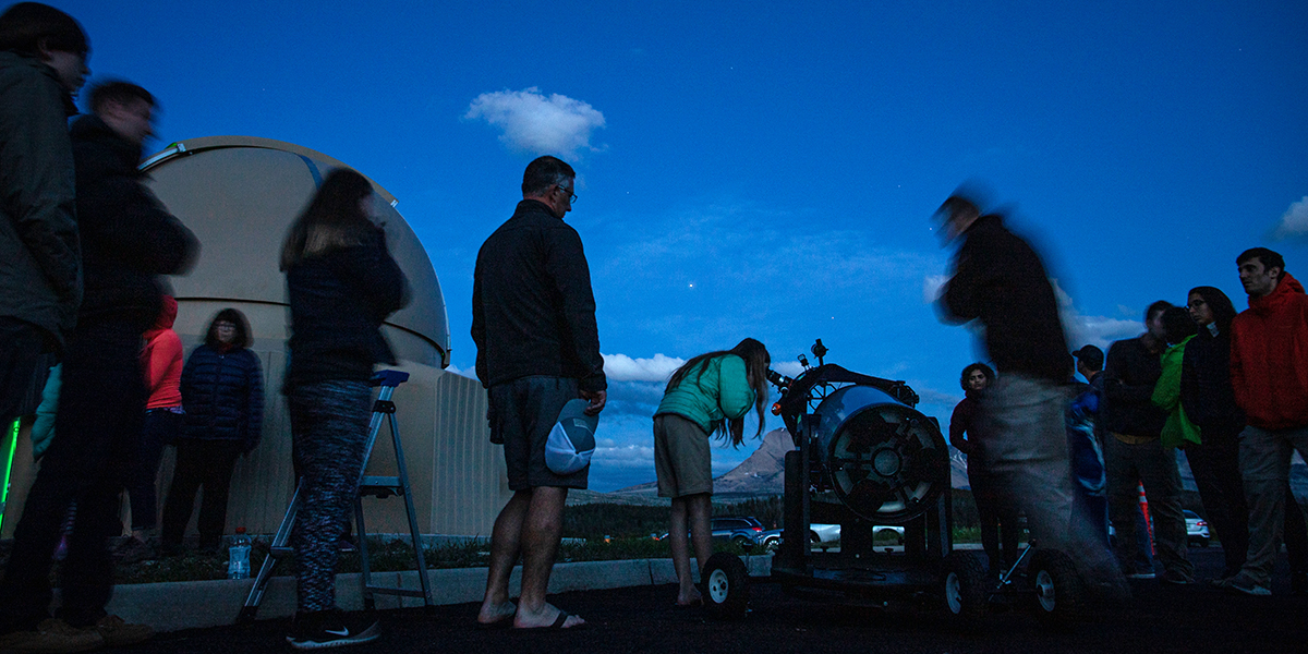 visitors look through a large telescope outside of the observatory at St. Mary