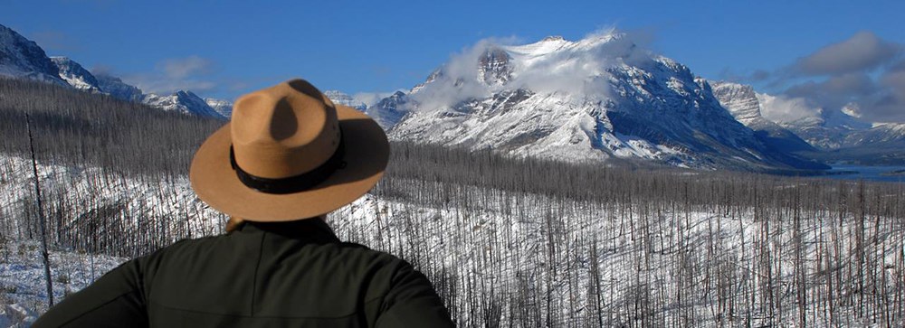 Ranger wearing flat hat faces snow covered mountain vista Ranger wearing flat hat faces snow covered mountain vista