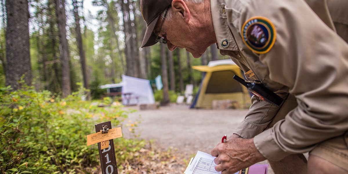 A campground host bends down to check on a campsite registration stub