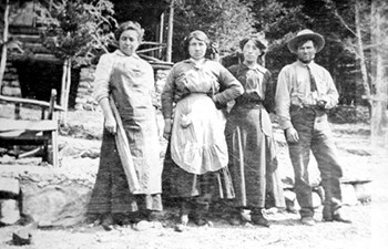 Historic image of man and three women in long skirts and aprons standing outside Historic image of man and three women in long skirts and aprons standing outside