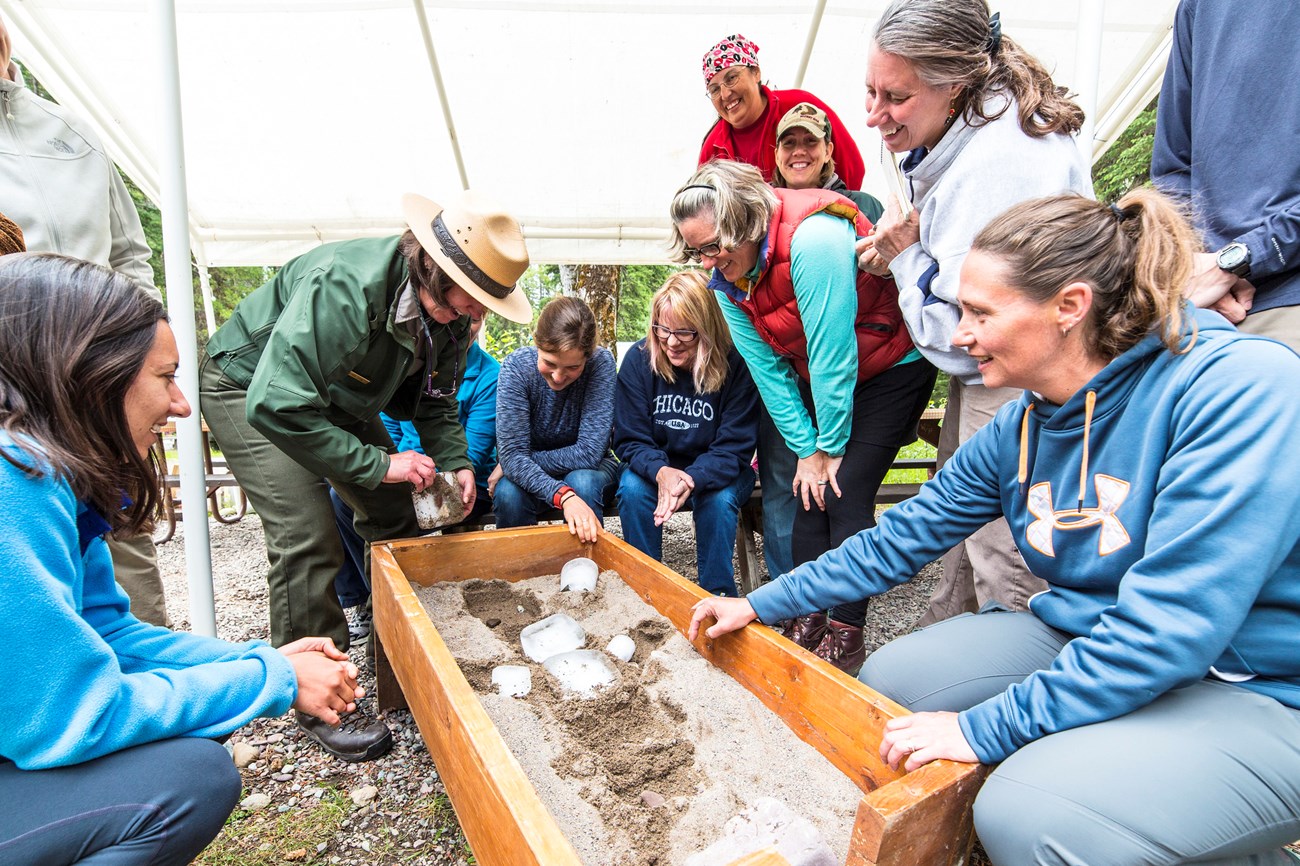 group of smiling women around a ranger and sandbox