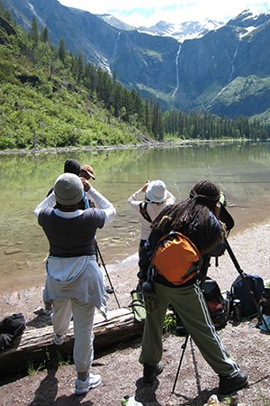 Students on lakeshore use scopes to look at huge rock wall at far end of lake