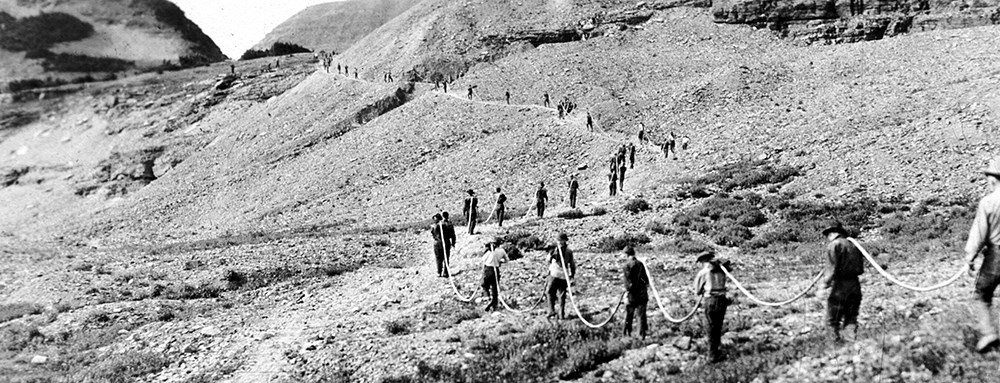 line of men carrying cord extends into distance