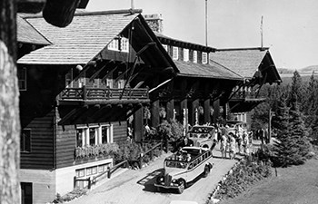 historic image of buses, people and grounds in front of wooden hotel with balconies