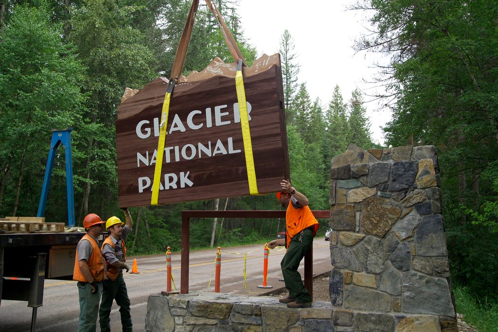 uniformed workers use crane truck to install wooden entrance sign