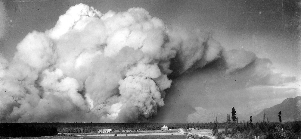 Historic image of huge smoke plum over tiny trees and buildings Historic image of huge smoke plum over tiny trees and buildings