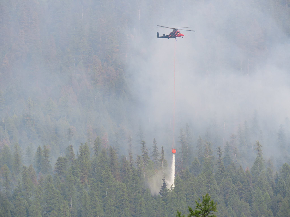 A helicoptor dangles a water bucket on a long line over forest fire A helicoptor dangles a water bucket on a long line over forest fire