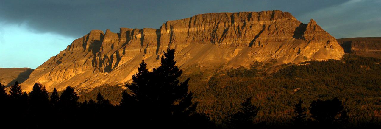 dark sky behind warmly lit, banded mountain ridge