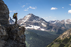 Backpacker stands on cliff edge looking upon mountain vista Backpacker stands on cliff edge looking upon mountain vista
