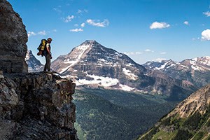 Backpacker stands on cliff edge looking upon mountain vista