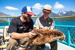 Ranger and Visitor sit on boat deck holding pelt