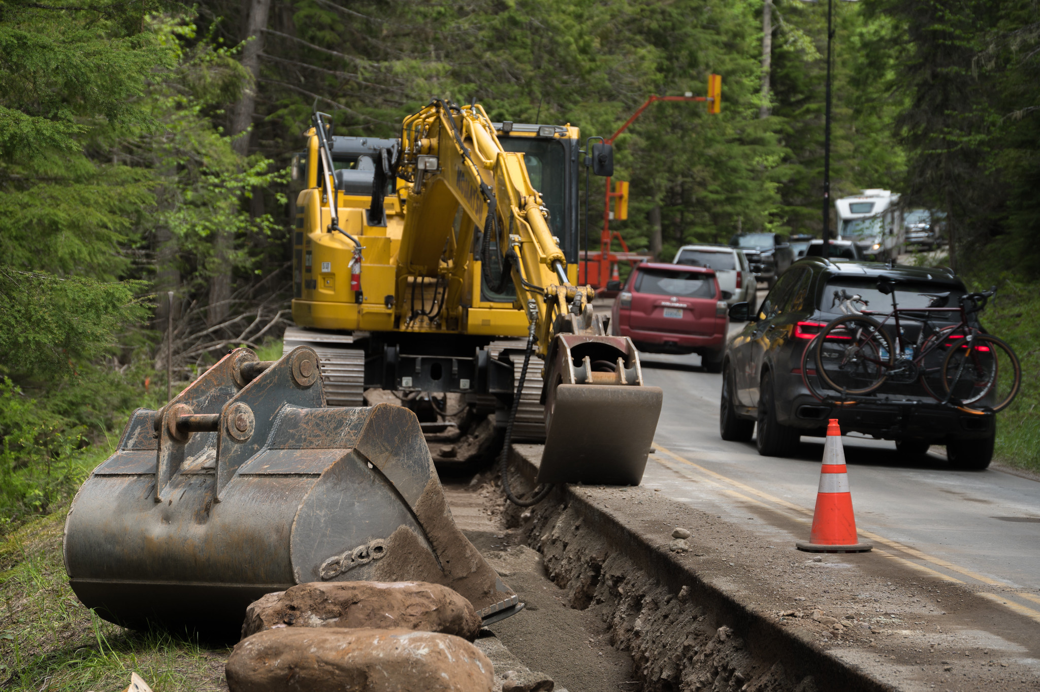 Lake McDonald Utilities Project Road construction equipment parked on Going-to-the-Sun Road near Lake McDonald. Cars driving by in opposite lane.