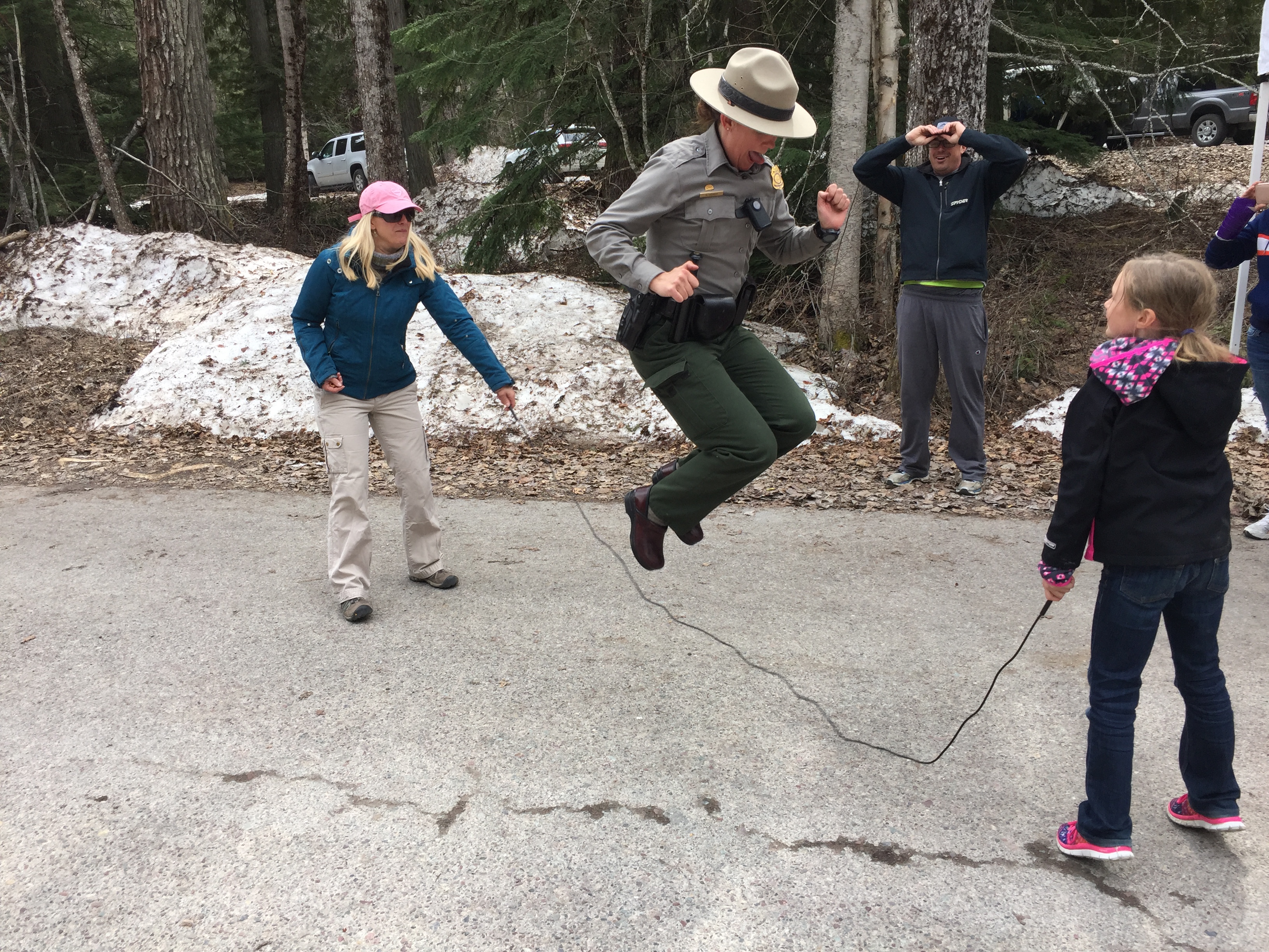 A park ranger wearing a flat hat jumps rope with two visitors.