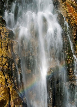 water falling over rocks with rainbow in droplets water falling over rocks with rainbow in droplets