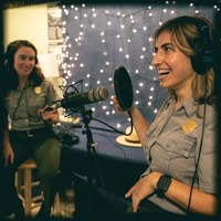 Two park rangers talk into microphones.