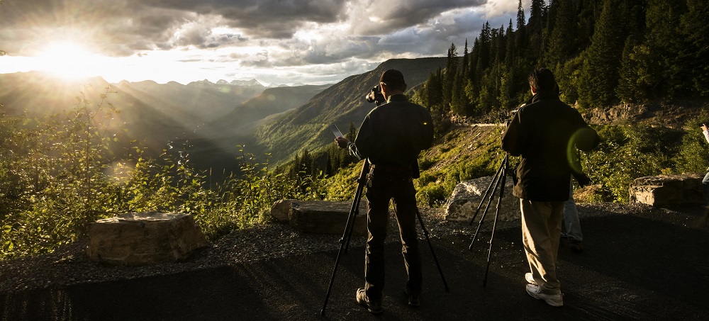 two photographers with tripods face a sunset over mountains two photographers with tripods face a sunset over mountains
