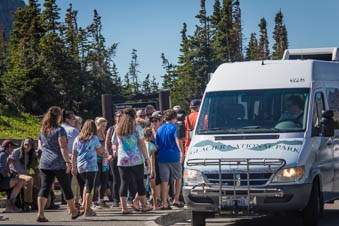 A crowd of people wait in a long line to board a shuttle bus.