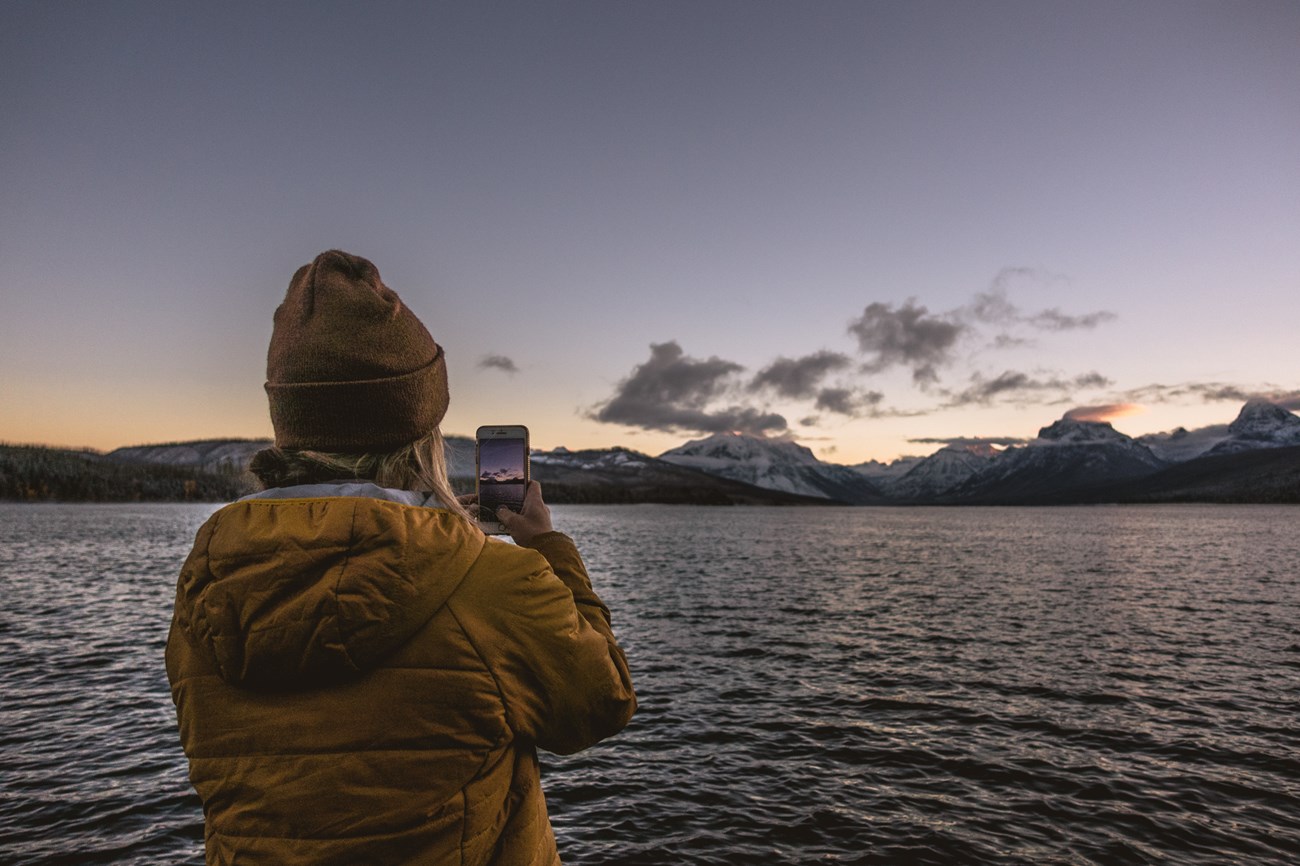 A person takes a picture with their phone in front of a lake.