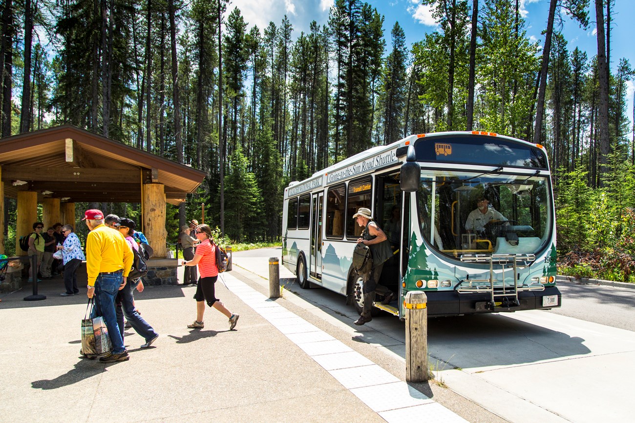 A shuttle is stopped at the Apgar Transit Center, letting visitors depart the shuttle. There is a group of people waiting to get on.