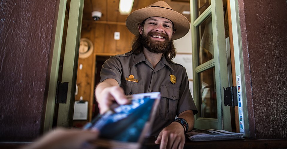 A ranger at an entrance station hands a Glacier pamphlet to a visitor.