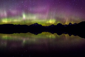 bands and glowing, colored lights in the sky over a silhouetted mountain range