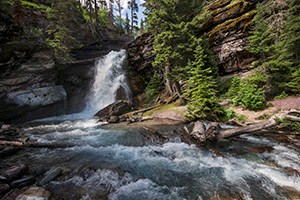 wide waterfall in forest setting falls into creek