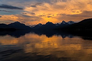 Golden clouds over silhouetted mountain range reflected in lake