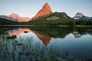 warm glow on mountain top reflected in cool lake surrounded by vegetation