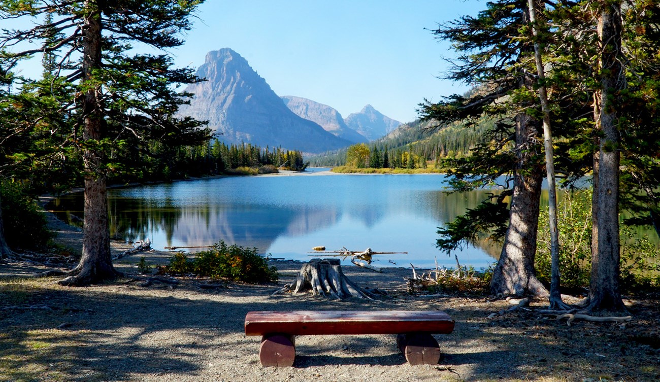 A picnic bench faces a small lake with mountains behind it.