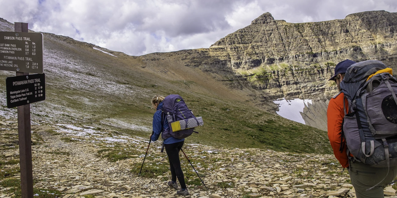 Wild Trip Planning Banner Two backpackers pass a trail junction sign on a ridgeline.