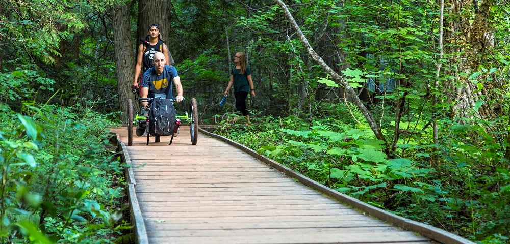 man with off-road wheelchair followed by visitors walking on boardwalk trail