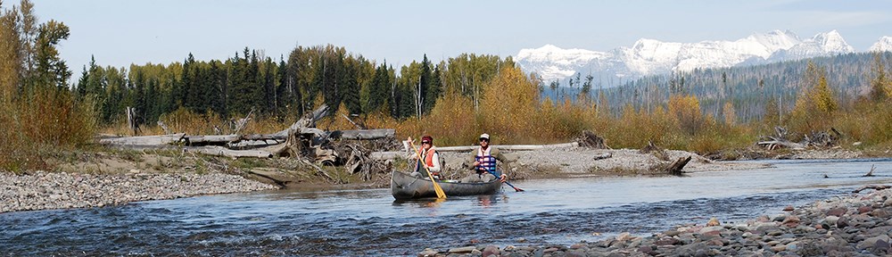 couple canoes past trees and rocky banks