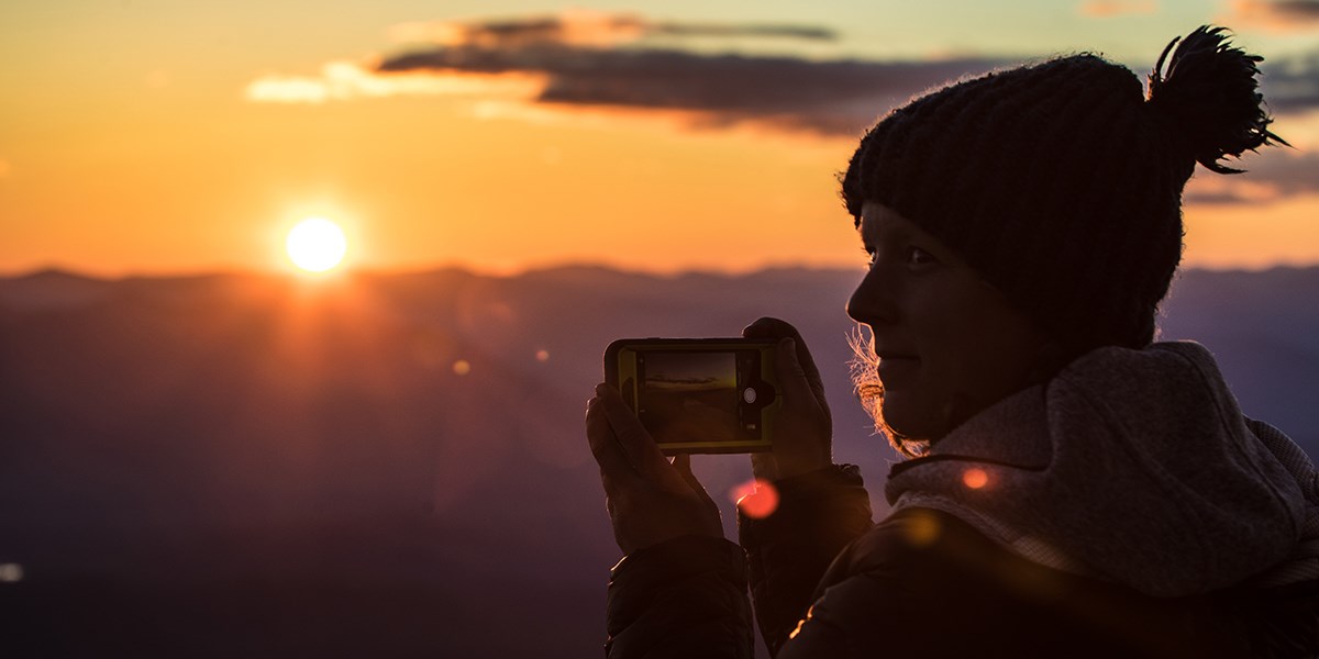 A hiker pauses to take a photo of a spectacular sunset to share online.