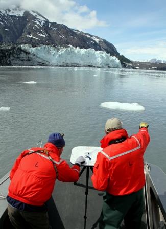 Two researchers look for murrelets in front of a glacier.