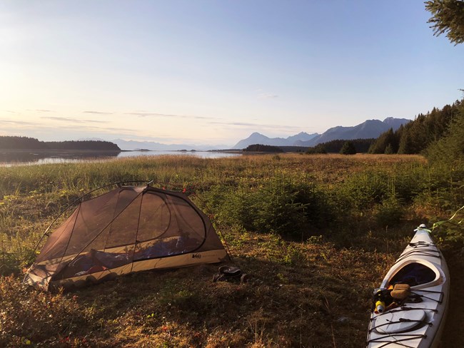 a tent set up on an island, surrounded by water and mountains and a pink sunset sky