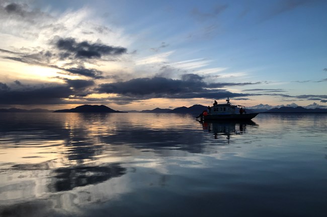 A park service boat on reflective water at sunset, the sky blue and orange colors.