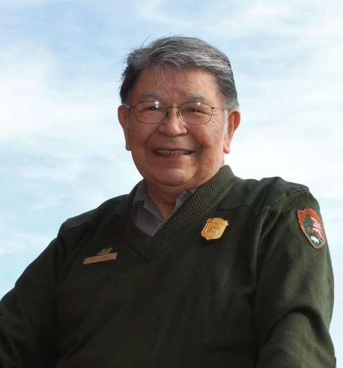 Elder Ken Grant smiles at the camera while wearing green and gold-accented NPS uniform