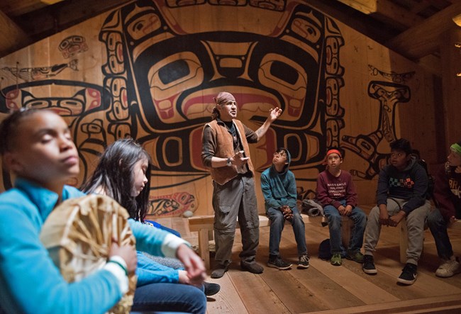 An elder speaks to listening youth inside the Huna Tribal House.