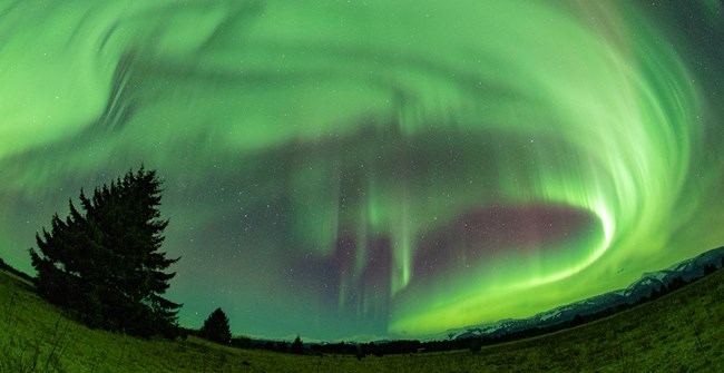 green aurora bands shine bright in a dark sky in curtain-like shapes.
