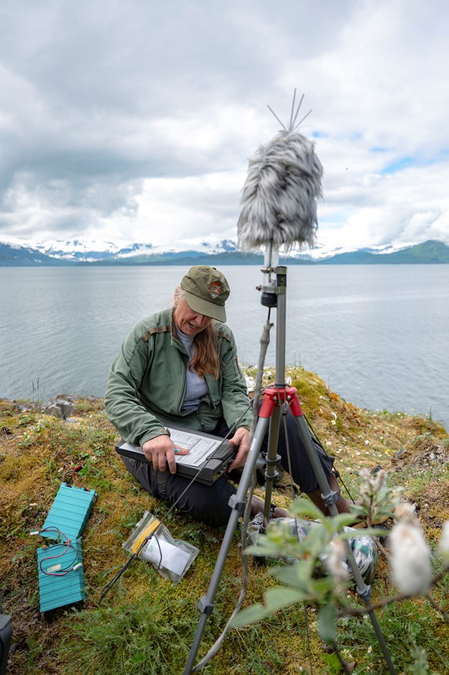 researcher takes notes next to a sound monitoring station on a tripod.