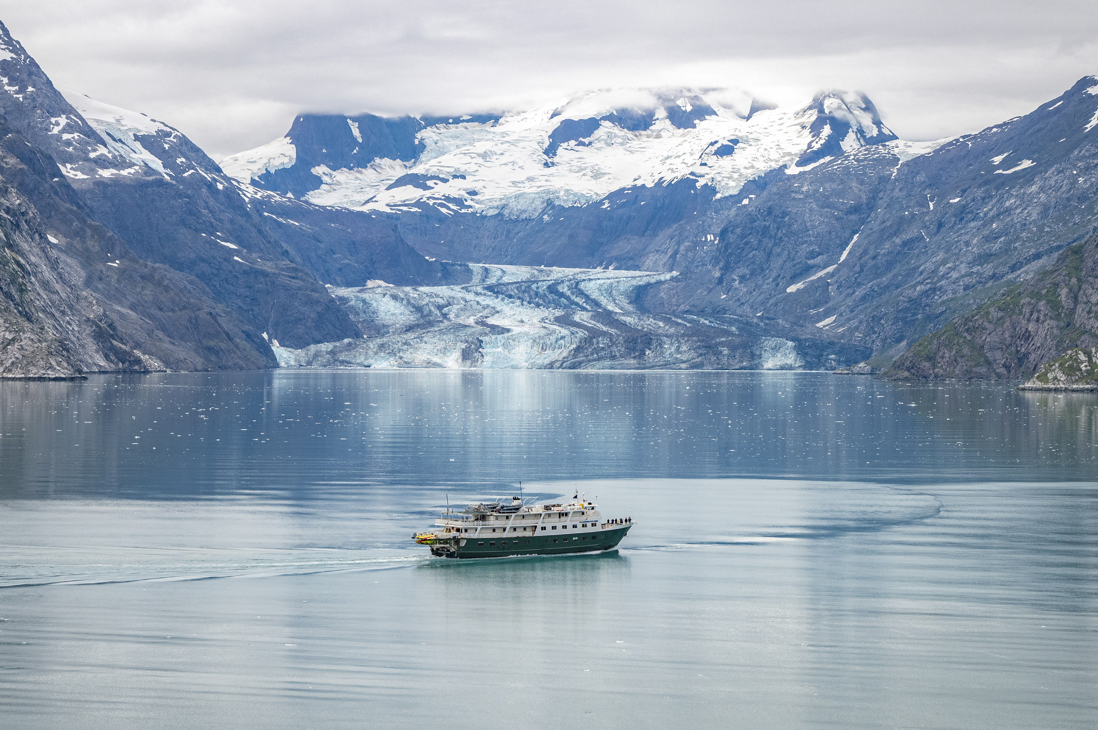 Tour Vessel in Johns Hopkins Inlet A tour vessel in the middle of a glacial fjord with snaking icy glacier in the distance.